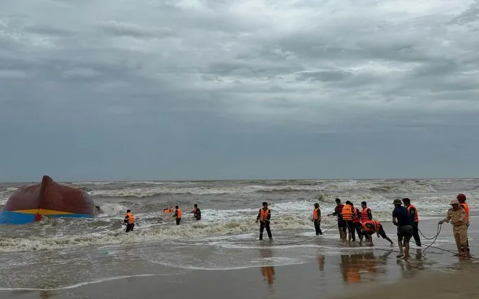 Lực lượng chức năng trục vớt một trong 2 tàu cá gặp nạn trôi dạt vào bờ (Nguồn: NLĐ)